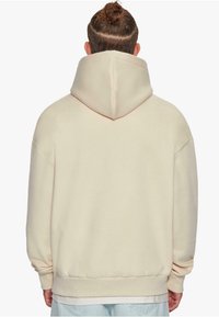 Cream-colored hooded sweatshirt with a relaxed fit, large back pocket, and ribbed cuffs. Smooth texture, minimalistic design.