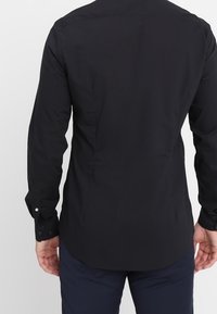 Zwarte longsleeve shirt met een getailleerde pasvorm. Heeft een soepele textuur, een afgeronde zoom en geplaatste manchetten. Geen patronen of zichtbare logo's.