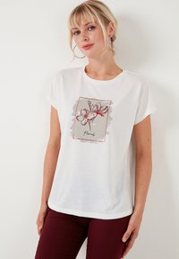 Witte t-shirt met korte mouwen, voorzien van een bloemig grafisch ontwerp in rood en grijs met een rechthoekige rand. Gemaakt van zacht, lichtgewicht stof.