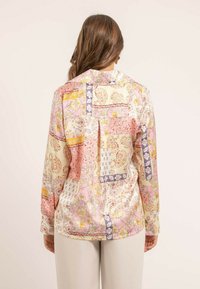 Chemise en satin avec un design en patchwork aux couleurs pastel, ornée de motifs floraux et cachemires. Tissu léger avec une coupe décontractée.