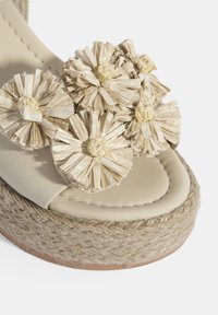 Beige platform sandaal met strooien bloemenaccenten, een gestructureerde jute-wrappingzool en een glad leren bovenwerk. Rondneus ontwerp.
