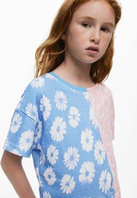 Kék és rózsaszín, rövid ujjú póló fehér virág- és absztrakt mintákkal; puha textúrával és kerek nyakkal.