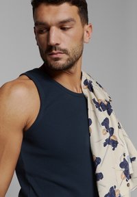 Marineblauw geribd hemd met een lichte sjaal met bloemenpatronen in marineblauw en beige. De sjaal hangt over de schouder.