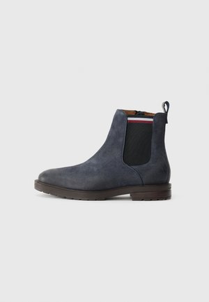 Botas Chelsea de ante navy con paneles laterales elásticos, una lengüeta y suela de goma marrón. Acabado texturizado y diseño minimalista.