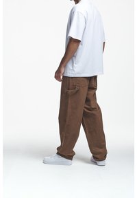 Biała koszulka z krótkim rękawem w połączeniu z luźnymi brązowymi spodniami i białymi trampkami, prezentująca prosty design i swobodny krój.