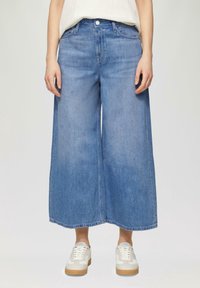 Leveälahkeiset siniset farkkukulotit, joissa on korkea vyötärö, edessä nappikiinnitys ja kaksi sivutaskua, yhdistettynä valkoisiin lenkkareihin.