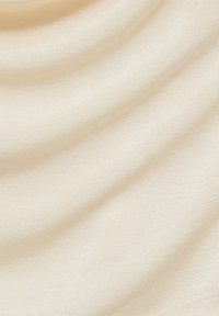 Tissu texturé beige clair avec un subtil éclat, présentant de doux plis et une surface lisse qui suggère un matériau léger.