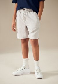 Lekkie szare lniane szorty z elastycznym paskiem i ozdobnym guzikiem, zestawione z białymi trampkami i białymi prążkowanymi skarpetami.