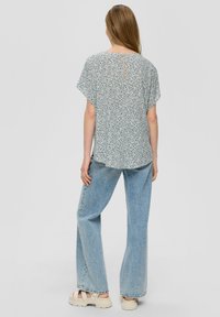 Bluse mit Blumenmuster in hellen Farben, lockerer Schnitt und Ausschnitt mit Schlitz im Rücken. Kombiniert mit weit geschnittenen Jeans in hellem Waschung und klobigen Sandalen.