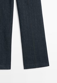Dunkelblaue Denim-Hose mit geradem Schnitt, sichtbaren Nähten entlang der Nähte und einer glatten Textur.