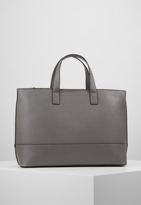 Bolsa tote gris con una superficie texturizada, dos asas cortas y una forma estructurada. Presenta una base negra contrastante en la parte inferior.
