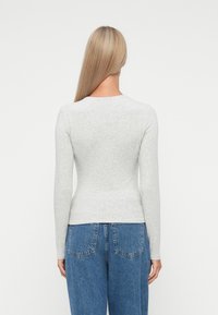 Hosszú ujjú, testhez simuló szürke felső, puha anyagból készült, kerek nyakkivágással. Magashegű kék denim farmernadrággal viselve, amelynek hátsó zsebei vannak.