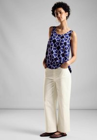 Marinblå och vit mönstrad ärmlös blus som är kombinerad med krämfärgade vida byxor och svarta platta skor, med avslappnad passform och definierad midja.