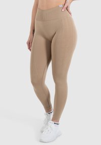Beige højtaljede leggings med ribbet talje, der har subtil tekstur og synlige detaljer, parret med hvide træningssko.