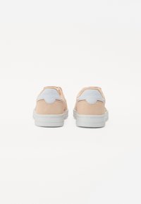 Persiske sneakers i ruskind med hvid hæltab, der har en tekstureret finish og en ridset hvid sål. Brandlogo synligt på hælen.