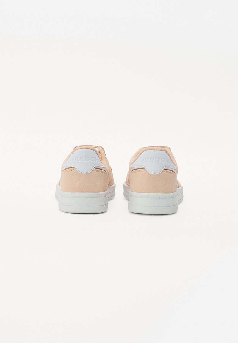 Zapatillas de ante melocotón con una pestaña blanca en el talón, que presentan un acabado texturizado y una suela blanca estriada. Logotipo de la marca visible en el talón.