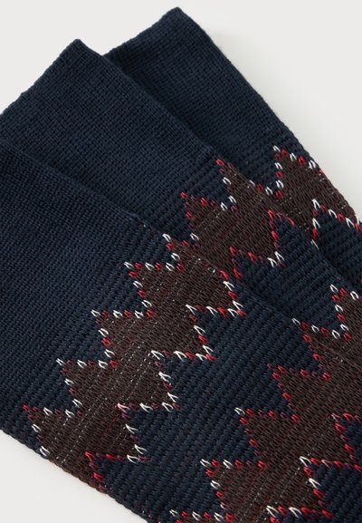 Chaussettes tricotées bleu foncé avec des motifs géométriques en zigzag marron, rouge et blanc.