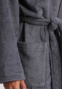 Szary bawełniany szlafrok z wiązanym paskiem w talii, o teksturowanej powierzchni i przedniej kieszeni. Posiada długie rękawy i luźny krój.