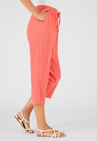Pantaloni capri a pieghe color corallo con cintura elastica e cordino, dotati di tasche laterali. Abbinati a sandali bianchi flat.