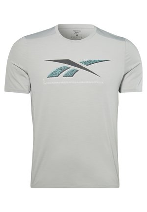 Homme portant un t-shirt blanc Reebok, un short bleu clair éclaboussé, des chaussettes noires Reebok et des chaussures de sport noires, bras tendus dans une pose de fitness.