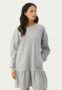 Graues Sweatshirt-Kleid mit langen Ärmeln, rundem Ausschnitt, seitlichen Taschen und gestuften, rüschierten Saum. Aus weicher, strukturiertem Stoff gefertigt.