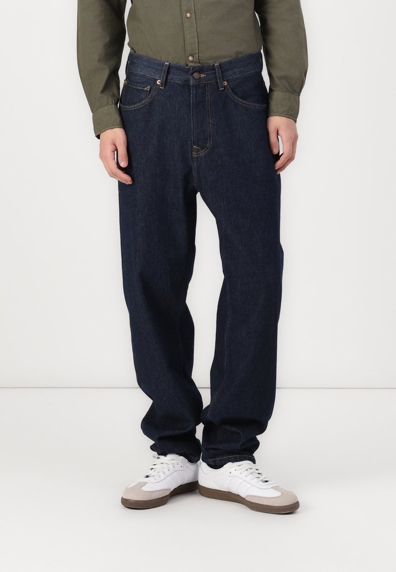 Mørkeblå denim jeans til mænd med en afslappet pasform, der har dobbelte lommer og kontrastsyninger, båret med hvide sneakers.