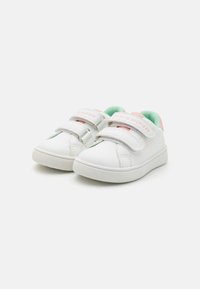 Weiße Sneaker mit einer weichen Textur, ausgestattet mit zwei Klettverschlüssen, pastellfarbenen Akzenten und einem mintgrünen Futter. Logo auf dem Riemen angebracht.