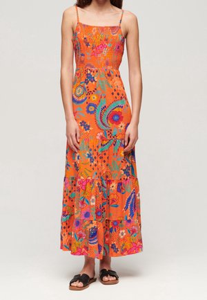 Sukienka maxi na cienkich ramiączkach w jaskrawym pomarańczowym kolorze, zdobiona misternymi kwiatowymi i geometrycznymi wzorami, z falbanami na dole i lekkim materiałem.