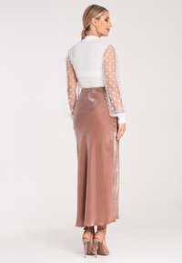 Langer, brauner Satinrock kombiniert mit einer weißen, transparenten Bluse mit Punkten. Die Bluse hat Puffärmel und eine taillierte Taille.