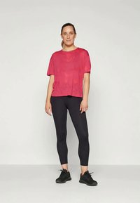 Rosa kortärmad topp med en något lös passform, i kombination med svarta leggings. Materialet verkar mjukt och lätt, vilket gör det lämpligt för träningskläder.