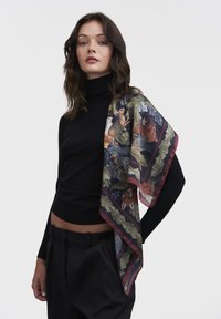 Svila šal z cvetnimi in živalskimi vzorci v bogatih barvah, obrobljen s temno rdečo. Nenasilno nosen čez črn pulover s turtleneck izrezom.