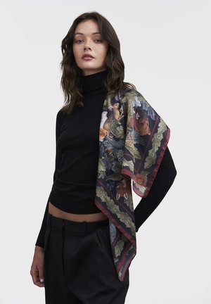 Seidenschal mit floralen und tierischen Mustern in reichen Farben, umrandet von Dunkelrot. Lässig über einem schwarzen Rollkragenoberteil getragen.