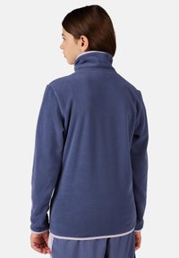 Modrý fleecový svetr s vysokým límcem, dlouhými rukávy a texturovaným povrchem. Lem má kontrastní světlou ozdobu.