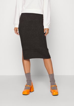 Grau gestrickter Midi-Rock mit gerippter Textur, kombiniert mit orangen Plateauschuhen und grauen Socken. Der Rock hat seitliche Schlitze am Saum.