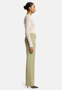 Lichtgewicht langemouwen top in zacht beige, gecombineerd met hoog getailleerde, rechte olijfgroene broek en zwarte pumps met stippen.