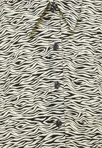 Chemise à motif zèbre noir et blanc, avec des boutons noirs sur le devant et un col pointu.