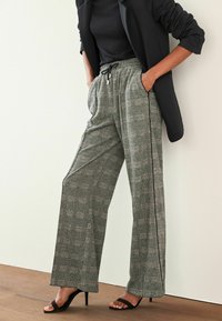 Grau karierte Hose mit lockerer Passform, elastischem Bund, seitlichen Taschen und schwarzen Seitenstreifen, kombiniert mit schwarzen Absätzen.