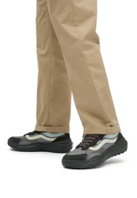 Black and gray sneakers with mesh and suede materials, featuring light blue accents, a textured sole, and brown laces. Tan pants in view.