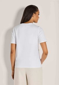 Witte korte mouw t-shirt met een ronde halslijn en een gladde textuur. De achterkant toont een minimalistisch ontwerp met een zijknopdetail.