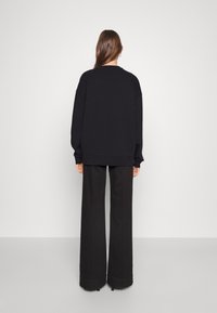 Svart oversized sweatshirt med rund halsringning, sänkta axlar och ribbade ärmslut, ihop med vida svarta byxor.
