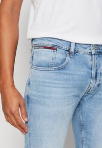 Ljusblå denimjeans med en smal passform. Har en klassisk femficksdesign, subtilt slitna partier och en kontrasterande accent i röd, vit och blå.