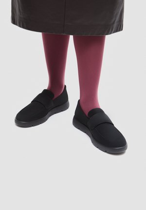 Legs wearing dark pink tights and black slip-on shoes, with a dark skirt hem visible above the knees, standing on a light background.