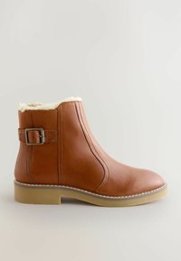 Bruine leren enkelboot met een crème fleece voering, zijgespelde riem en een gumrubberen zool op een neutrale achtergrond.