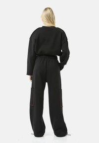 Zwarte cropped sweatshirt en bijpassende losse broek met elastische taille, voorzien van zijzakken en zichtbare stikseldetails.