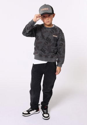 Sweatshirt de camouflage gris avec logo "HUGO", jeans noirs et baskets à motifs. Casquette noire et grise avec texte "HUGO".