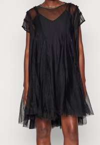 Czarna sukienka z przezroczystymi krótkimi rękawami, dekoltem w serek i warstwowym krojem. Miękka, lekka tkanina o subtelnej teksturze i płynnej sylwetce.