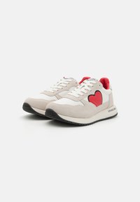 Μπεζ πάνινα sneakers με κόκκινη καρδιά, λευκές δερμάτινες λεπτομέρειες και μαύρη καουτσούκ σόλα. Διαθέτουν λευκές κορδόνες και λογότυπο στη φτέρνα.
