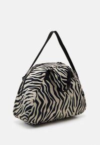 Bolso de viaje con estampado de cebra, hecho de tela, en colores negro y crema, con asas dobles y cierre de cremallera. Forma redondeada.
