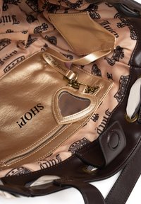 Brown leather handbag interior with a gold zipper pocket, light pink lining featuring black patterns, and a heart-shaped mirror keychain.