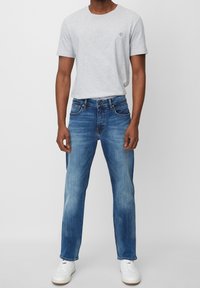 Camiseta de algodón gris de manga corta, combinada con jeans de mezclilla en un lavado azul medio que presentan un corte recto y detalles deslavados. Zapatillas blancas.